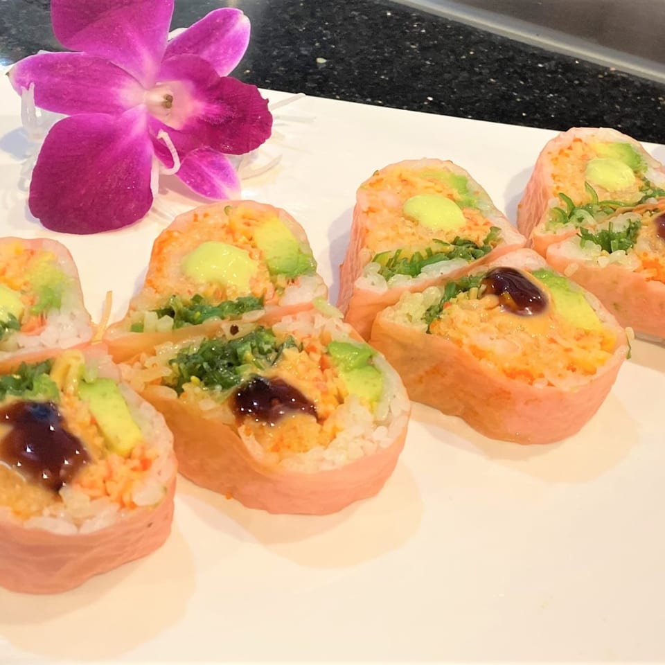 Pink sushi rolls with avocado, green garnish, and dark sauce, garnished with a purple orchid.
