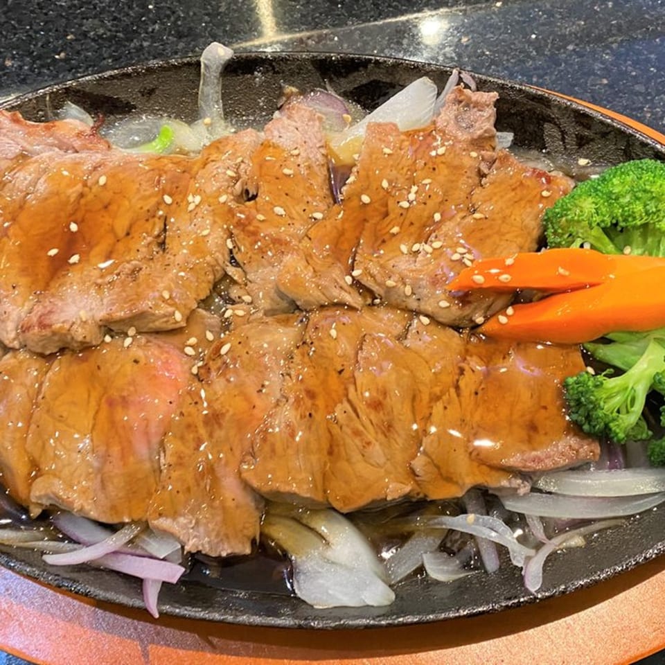 Sizzling teriyaki beef with sesame seeds, onions, broccoli, and carrots on a hot plate.
