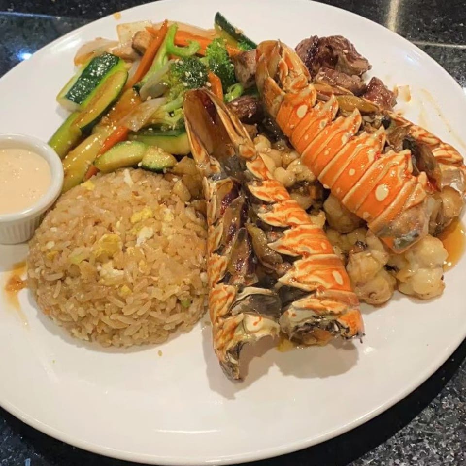 A Japanese hibachi dinner with lobster tails, fried rice, steak, and mixed vegetables.